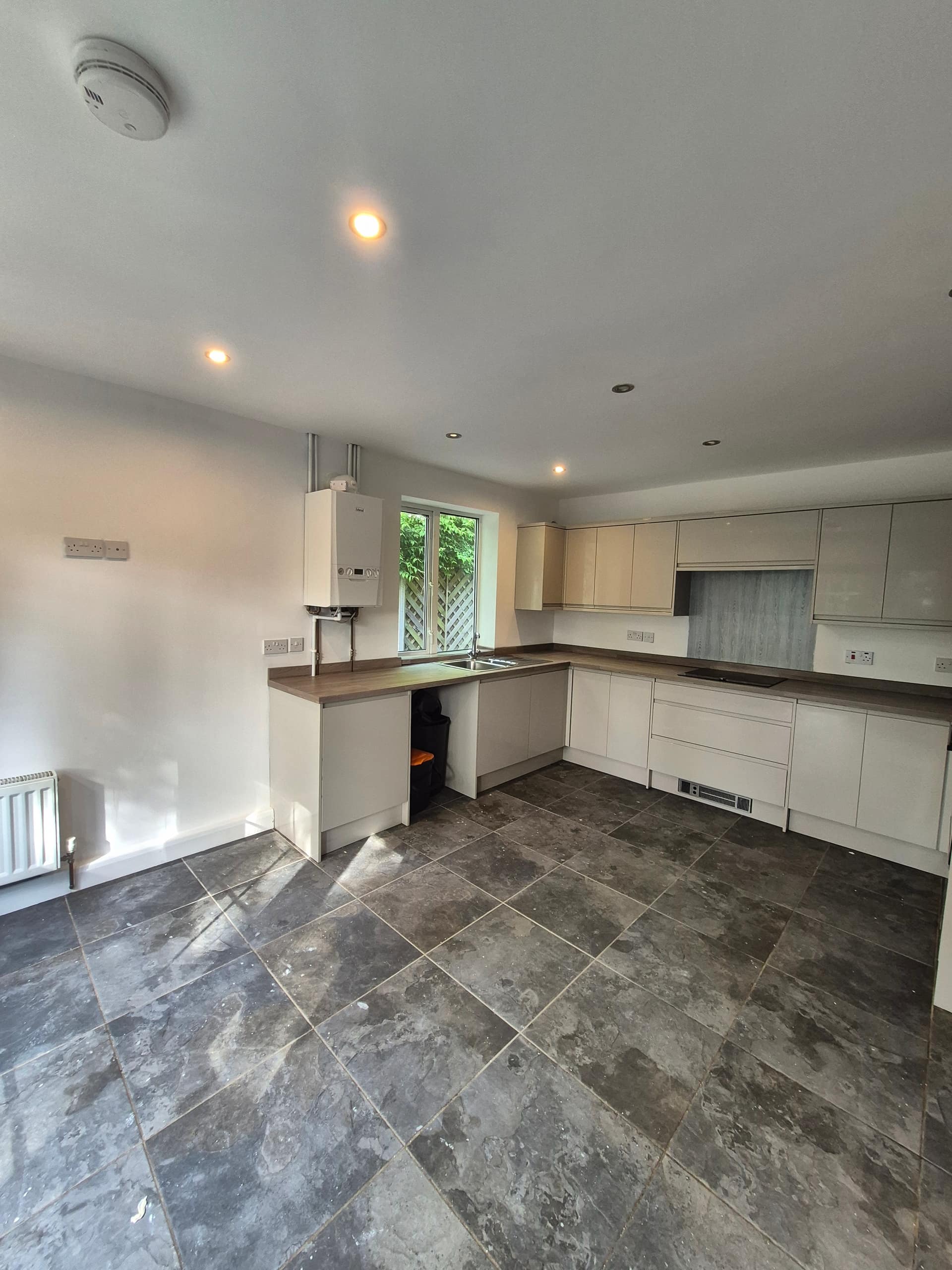 Newly fitted modern kitchen in a Lincoln rental property completed by LWR Group, with white gloss units, dark tile flooring, and recessed lighting, ready for tenants